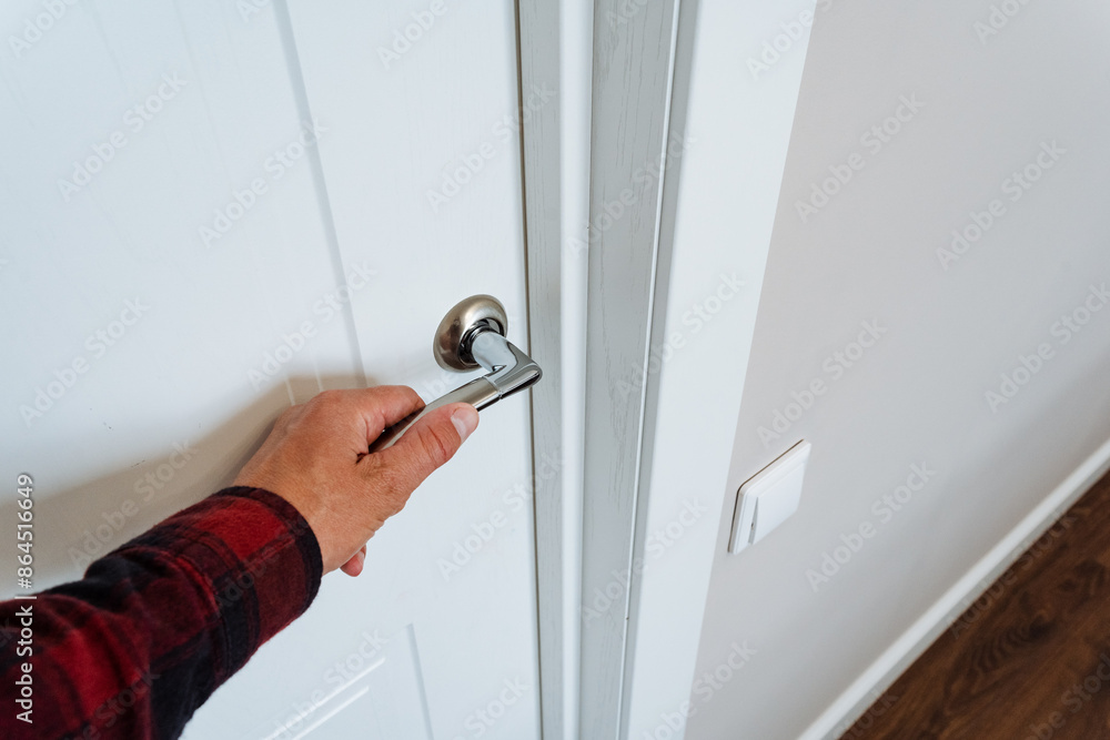 A person is opening a white door inside a home by using a door handle, possibly made of wood or glass. The home features a hardwood ceiling, creating a warm and inviting space A person is opening a white door inside a home by using a door handle, possibly made of wood or glass. The home features a hardwood ceiling, creating a warm and inviting space