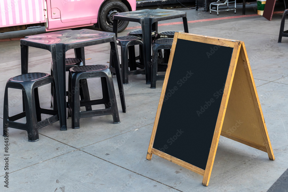 Empty chalkboard next to tables and chairs and a food truck in a square in Brazil