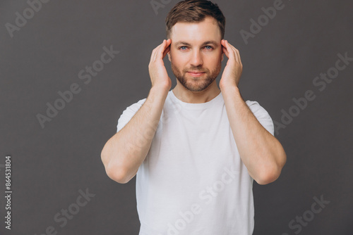 Cute bearded man massaging his scalp on gray background in studio, beauty and care concept