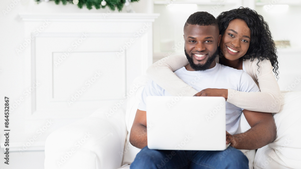 A happy couple sits on a white couch, the woman hugging the man from behind as they use a laptop. A happy couple sits on a white couch, the woman hugging the man from behind as they use a laptop.