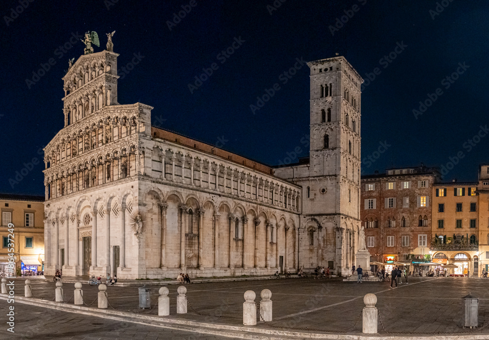 Obraz premium Night view of the San Michele in Foro church in Lucca, Italy, with surrounding buildings and a clear sky.