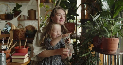 Wallpaper Mural Young loving mother and her adorable little daughter have fun spraying decorative plants with water in the home garden together. Family joint leisure. Torontodigital.ca