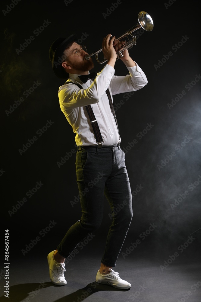 Professional musician playing trumpet on black background in color lights and smoke Professional musician playing trumpet on black background in color lights and smoke