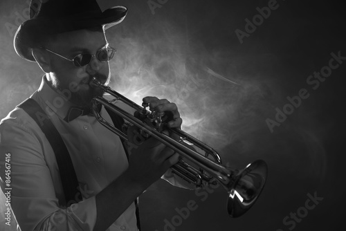 Professional musician playing trumpet on dark background with smoke, space for text. Black and white effect