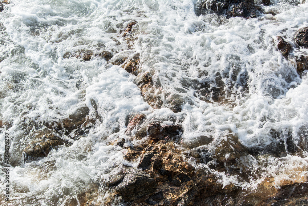 Obraz premium Beach water hitting the dark rocks.