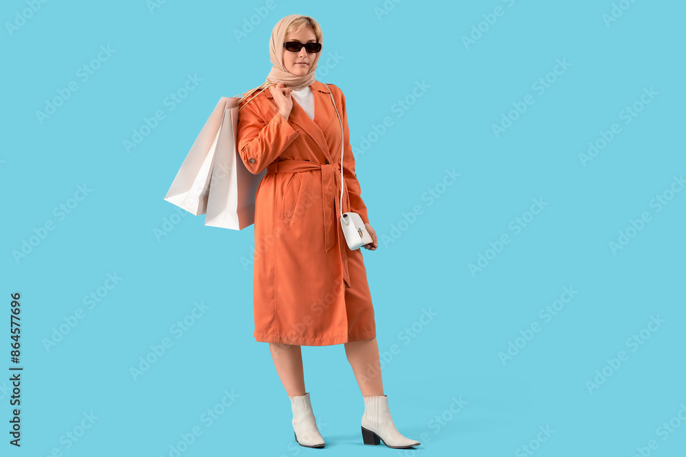Fototapeta premium Stylish beautiful young woman with shopping bags on blue background