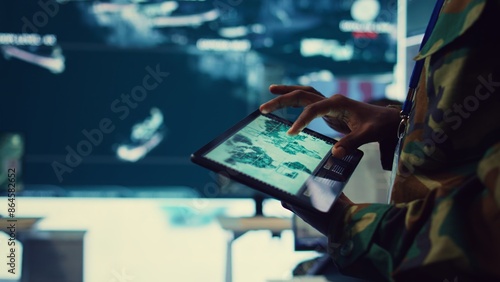 Fotografía Army soldier reviews targets on a satellite world map to ensure global protection, works on tablet in military command center