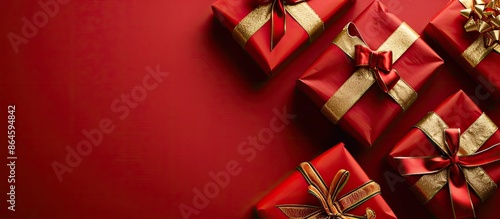 Gifts displayed elegantly on a red background adorned with gold and red ribbons, providing copy space image.