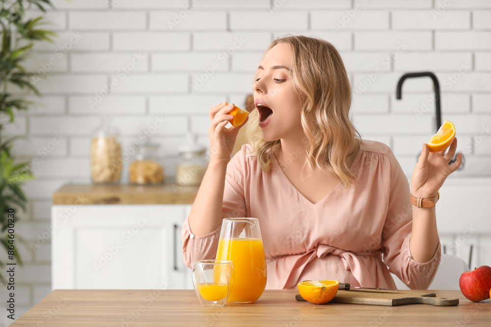 Young pregnant woman eating orange at table in kitchen Young pregnant woman eating orange at table in kitchen