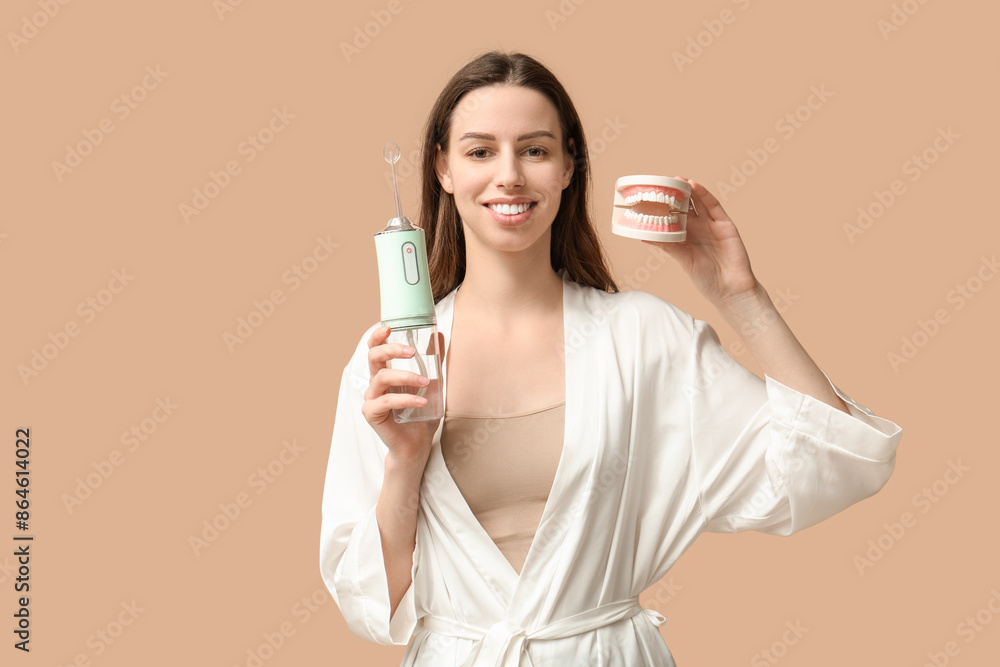 Beautiful young woman with oral irrigator and jaw model on brown background Beautiful young woman with oral irrigator and jaw model on brown background