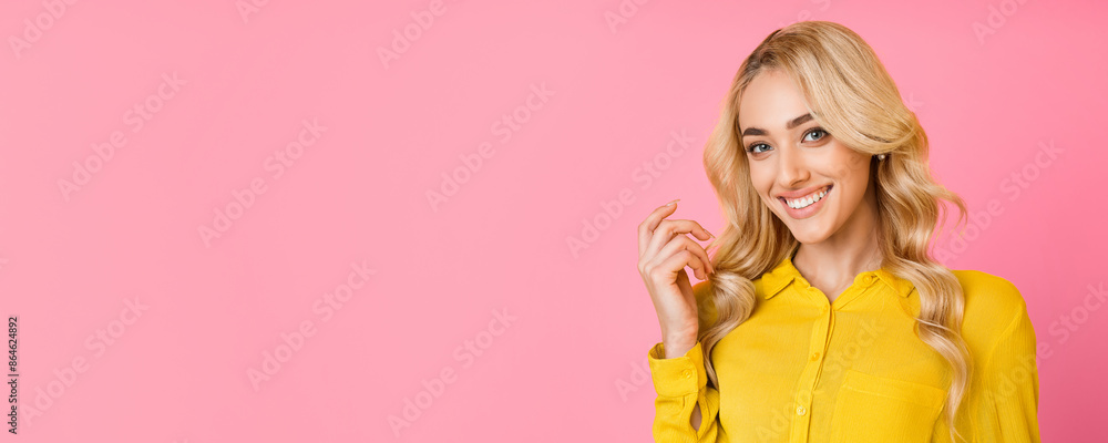 A young woman with blonde hair and a bright smile is pictured against a pink backdrop. She is wearing a yellow shirt and has her hand resting on her cheek, panorama with copy space A young woman with blonde hair and a bright smile is pictured against a pink backdrop. She is wearing a yellow shirt and has her hand resting on her cheek, panorama with copy space