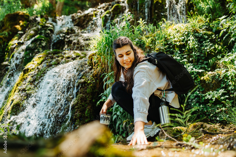 One young caucasian woman is taking a break from hiking near the river and waterfall in the forest One young caucasian woman is taking a break from hiking near the river and waterfall in the forest