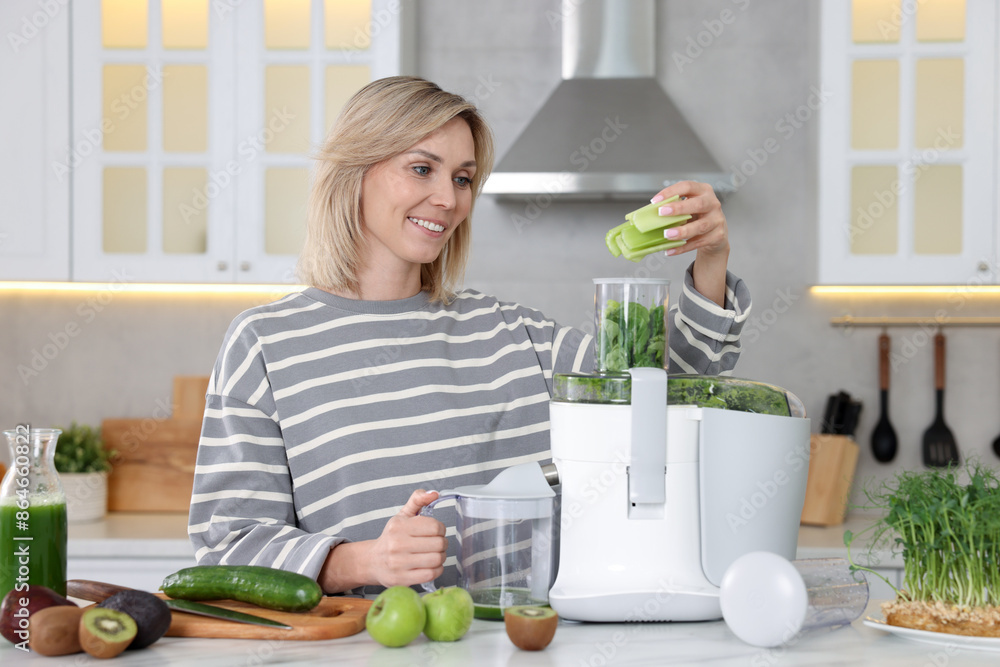 Smiling woman putting fresh celery into juicer at white marble table in kitchen Smiling woman putting fresh celery into juicer at white marble table in kitchen