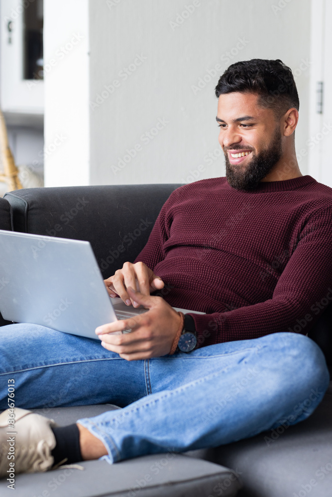 Smiling man using laptop while relaxing on couch at home Smiling man using laptop while relaxing on couch at home