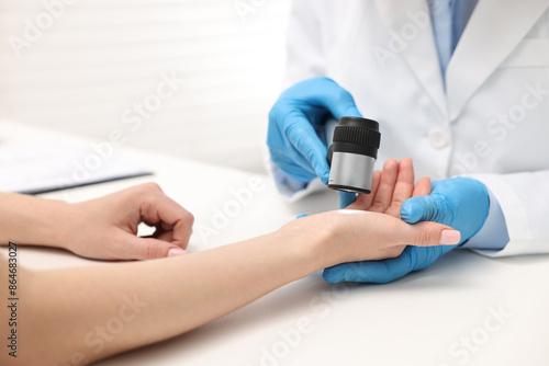 Dermatologist with dermatoscope examining patient at white table in clinic, closeup