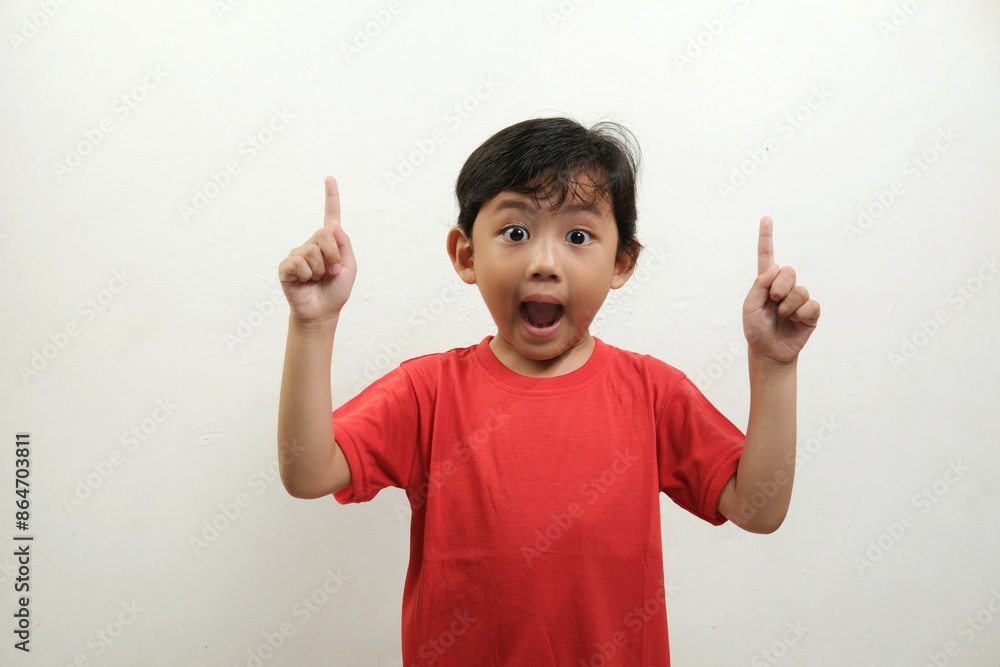 A surprised young boy in a red shirt points upward with both hands, his eyes wide open and mouth agape in astonishment.Perfect for concepts related to discovery,surprise, excitement,or learning moment A surprised young boy in a red shirt points upward with both hands, his eyes wide open and mouth agape in astonishment.Perfect for concepts related to discovery,surprise, excitement,or learning moment
