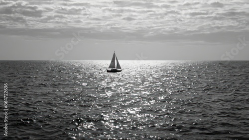 black and white photo of a lone sailboat in the middle of the ocean