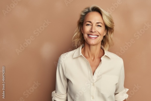 Portrait of smiling senior businesswoman standing against beige wall.
