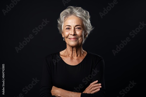 Portrait of a smiling senior woman standing with arms crossed against black background