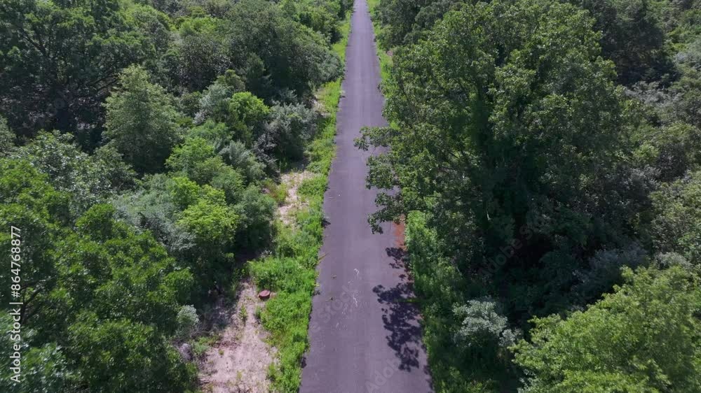 An aerial view of a narrow, paved road with green trees and bushes on either side. Taken on a sunny day, the drone camera is tilted down and dolly in over the road. An aerial view of a narrow, paved road with green trees and bushes on either side. Taken on a sunny day, the drone camera is tilted down and dolly in over the road.