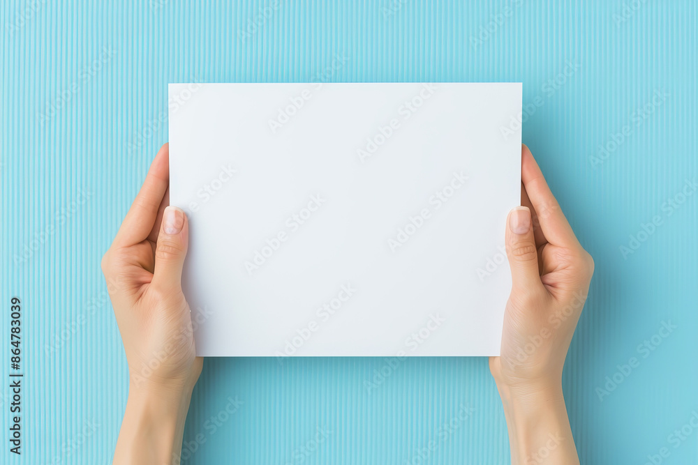 Hands holding a blank white paper on a blue background, perfect for mockups and presentations. Hands holding a blank white paper on a blue background, perfect for mockups and presentations.