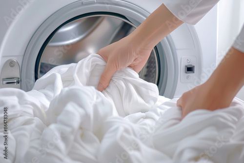 Hands loading white laundry into a washing machine. Concept of household chores and cleanliness with fresh, clean clothes.
