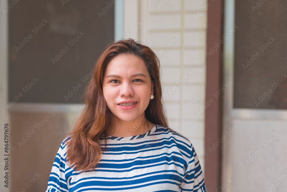Asian woman in her 30s standing outside her apartment flat, smiling at the camera. She has long hair and is wearing a striped shirt. Asian woman in her 30s standing outside her apartment flat, smiling at the camera. She has long hair and is wearing a striped shirt.