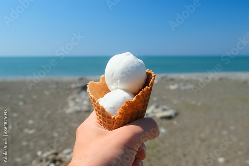 Hand of man holding ice cream on resort sea shore coast on blur background. Man resting relaxing on resort on vacation in sunny summer day. Travel, tourism, vacation, pleasure, enjoying.