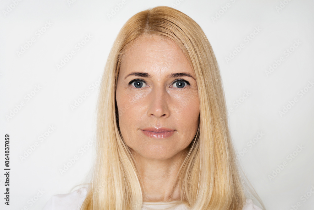 This image is a portrait of a woman with blonde hair and blue eyes. She is looking directly at the camera and has a neutral expression. She is standing in front of a white background. This image is a portrait of a woman with blonde hair and blue eyes. She is looking directly at the camera and has a neutral expression. She is standing in front of a white background.