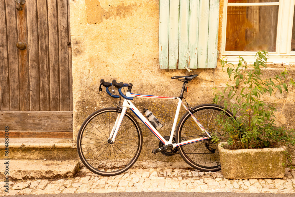 A bicycle (road bike) leans against an old, weathered house facade with a window and front door with wooden shutters in Saignon, a high-altitude village in the Luberon, Provence, France A bicycle (road bike) leans against an old, weathered house facade with a window and front door with wooden shutters in Saignon, a high-altitude village in the Luberon, Provence, France