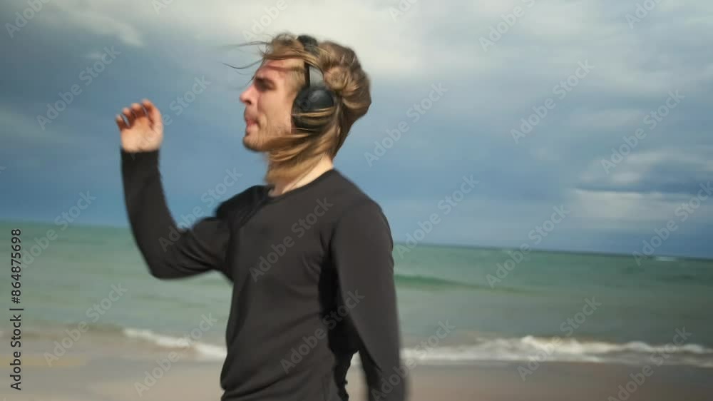 Smiling young man in black clothes dancing moving his arms on the beach in a positive mood listening to music on headphones enjoying nature. Smiling young man in black clothes dancing moving his arms on the beach in a positive mood listening to music on headphones enjoying nature.