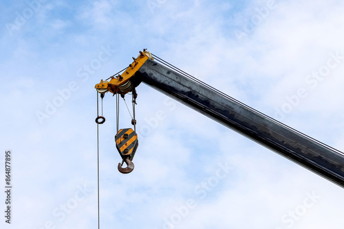 Closeup of an old lifting hook attached to sheave suspended by wire rope from boom of crane against the sky