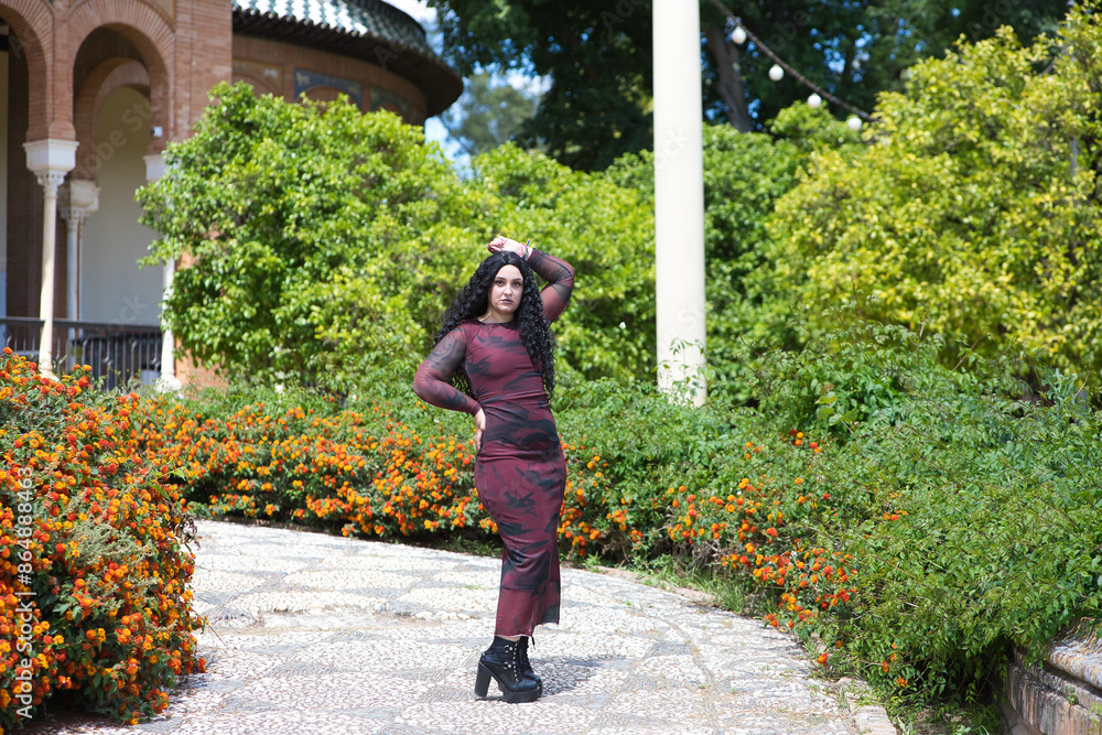 Fototapeta premium young and beautiful latin woman, brunette with curly hair, walks among the vegetation and buildings of a famous park in spain. The woman is on holiday in seville and enjoys the sunshine.
