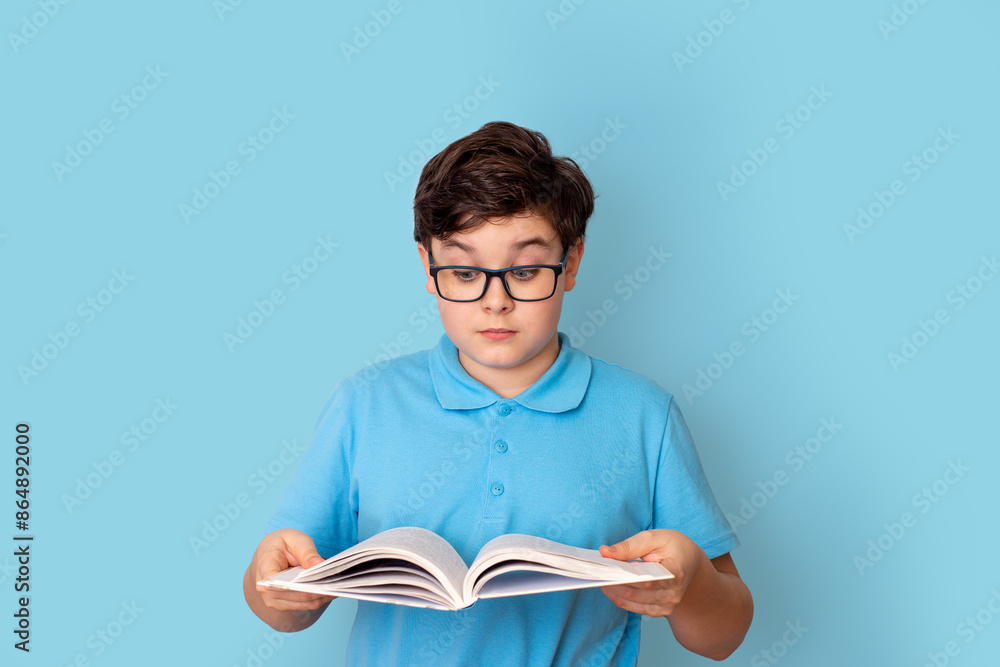 A surprised schoolboy in glasses, holding an open book in his hands, he looks at it A surprised schoolboy in glasses, holding an open book in his hands, he looks at it