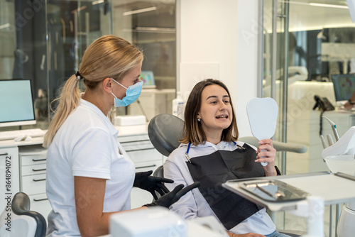 female dentist and patient smiling and looking at their white teeth in mirror while sitting © RomanR
