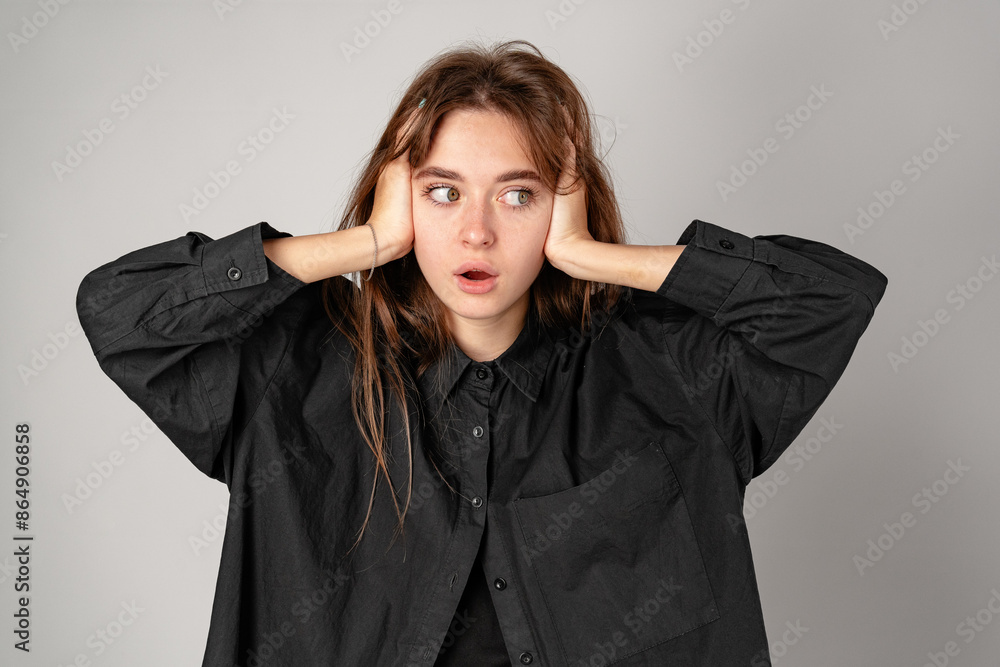 Young Woman With Surprised Expression Holding Head Against a Gray Background Young Woman With Surprised Expression Holding Head Against a Gray Background