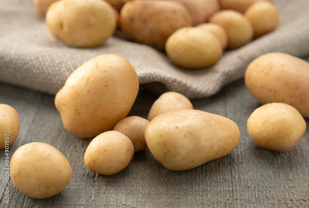 Young clean potatoes lie scattered on a wooden background with jute cloth, bag Young clean potatoes lie scattered on a wooden background with jute cloth, bag