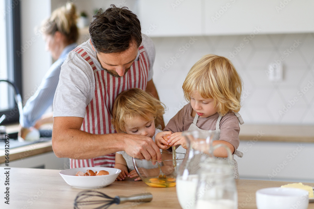 Young nuclear family making pancakes together. Parents and children in kitchen, preparing pancake batter, spending weekend day indoors. Young nuclear family making pancakes together. Parents and children in kitchen, preparing pancake batter, spending weekend day indoors.