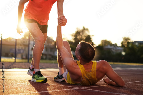 One athlete helps another to stand up after being injured while running at the stadium