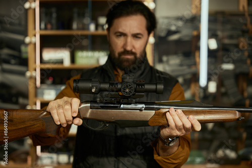 Mature man seller demonstrating gun standing at counter desk in weapon shop