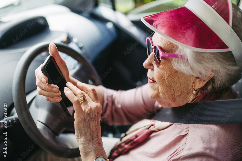 Happy senior woman driving car alone, holding smartphone and scrolling ...