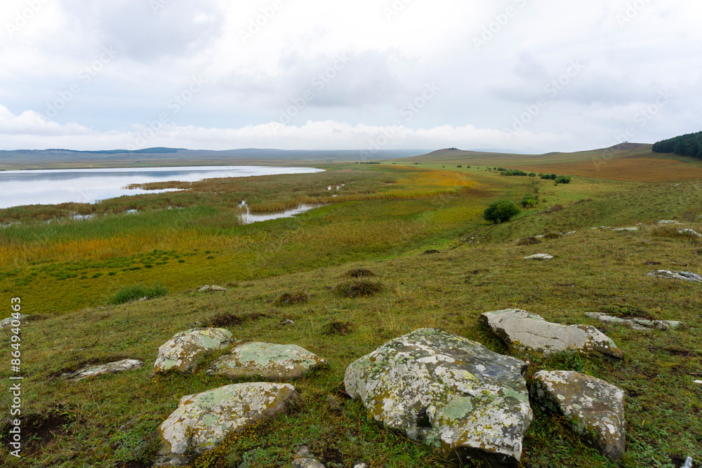 Huge rocks with moss in the foreground. Part of Bareti lake surrounded by fields of faded and green grass. Huge rocks with moss in the foreground. Part of Bareti lake surrounded by fields of faded and green grass.