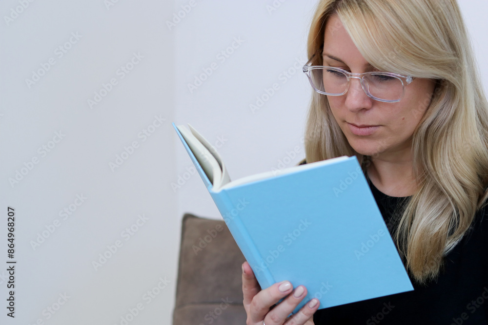 Close up portrait of a caucasian millennial female with glasses siting on a couch and reading a book Close up portrait of a caucasian millennial female with glasses siting on a couch and reading a book