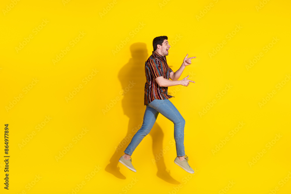 Full size photo of nice young man jump indicate fingers empty space wear shirt isolated on yellow color background Full size photo of nice young man jump indicate fingers empty space wear shirt isolated on yellow color background