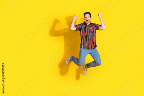 Full size photo of nice young man jump raise fists wear shirt isolated on yellow color background