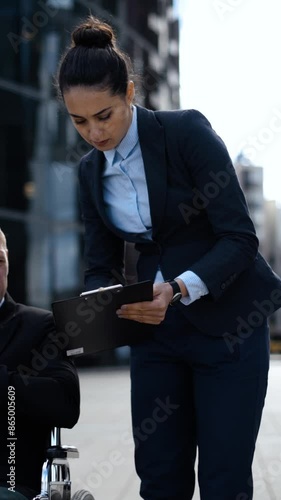 Young entrepreneur cripple business man in invalid wheelchair communicates with his woman lady colleague secretary assistant about documents in textpad. Vertical shot. photo