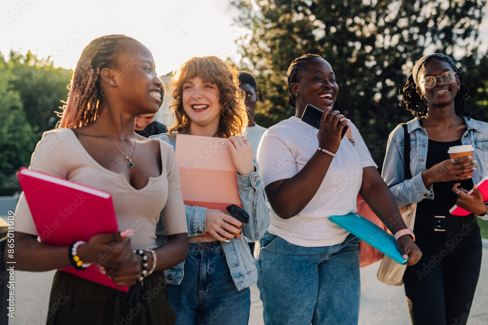 Fototapeta premium Happy diverse college girls at campus walking with textbooks in hands.