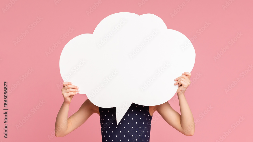 Little girl hiding her face behind blank white speech bubble, pink studio background Little girl hiding her face behind blank white speech bubble, pink studio background