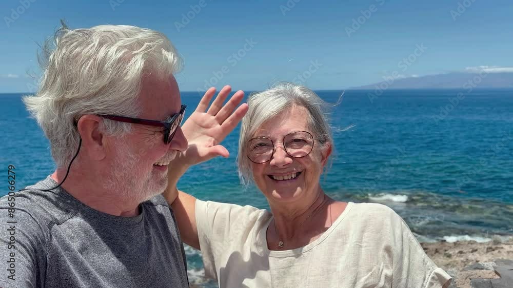 Smiling senior couple walks along sea coast enjoying summer vacation and looks towards camera expressing happiness and freedom, capturing a moment of joy, horizon over the sea Smiling senior couple walks along sea coast enjoying summer vacation and looks towards camera expressing happiness and freedom, capturing a moment of joy, horizon over the sea