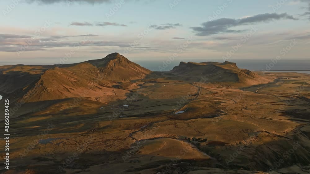 Aerial view of Mýrdalur, Iceland, showcasing rugged coastal hills bathed in sunset light with winding roads and expansive views Aerial view of Mýrdalur, Iceland, showcasing rugged coastal hills bathed in sunset light with winding roads and expansive views